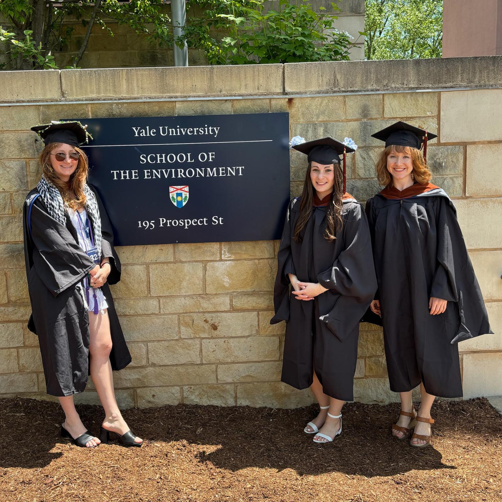 Three graduates posing in front of a sign at Yale University