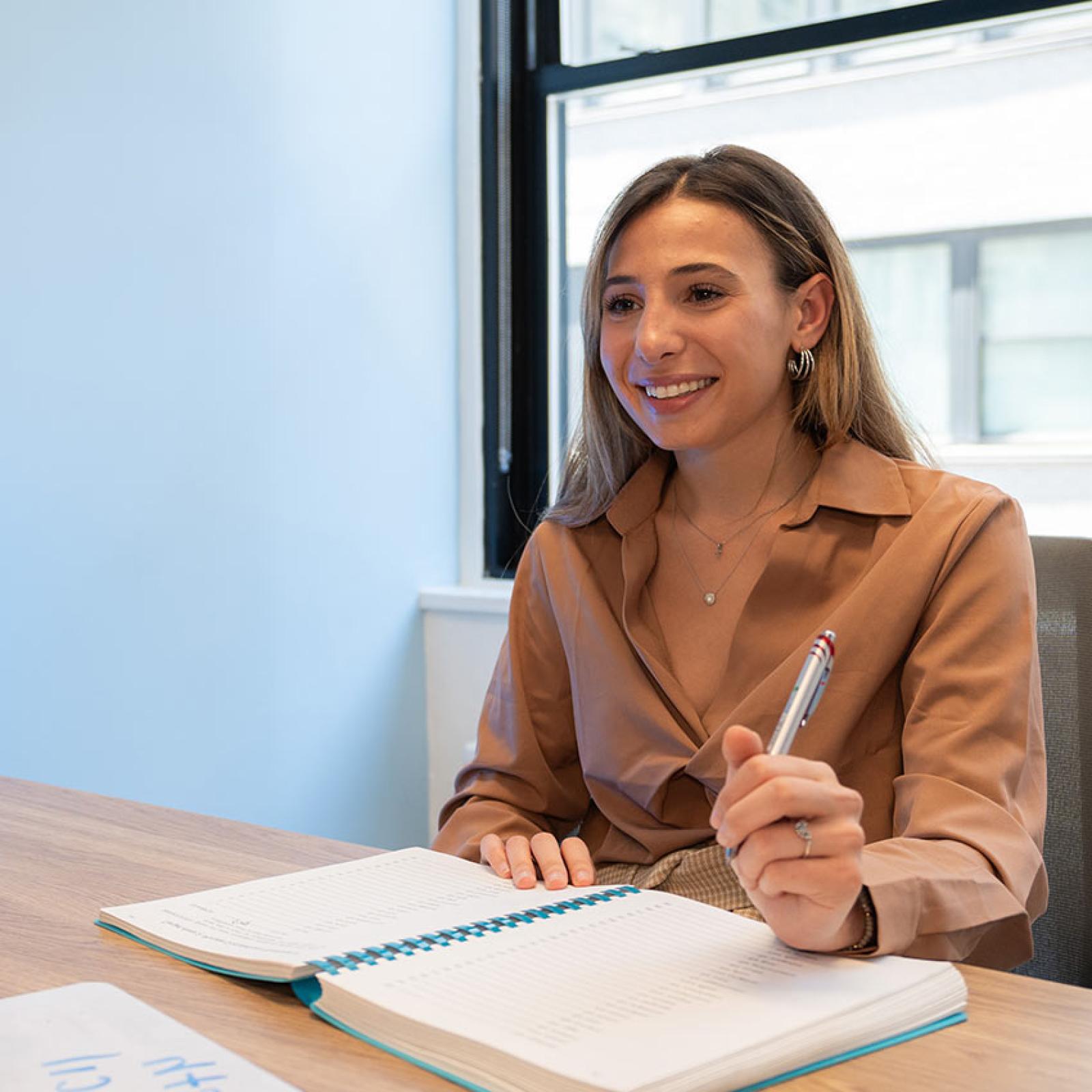 A Pace University student holds a pen over a notebook