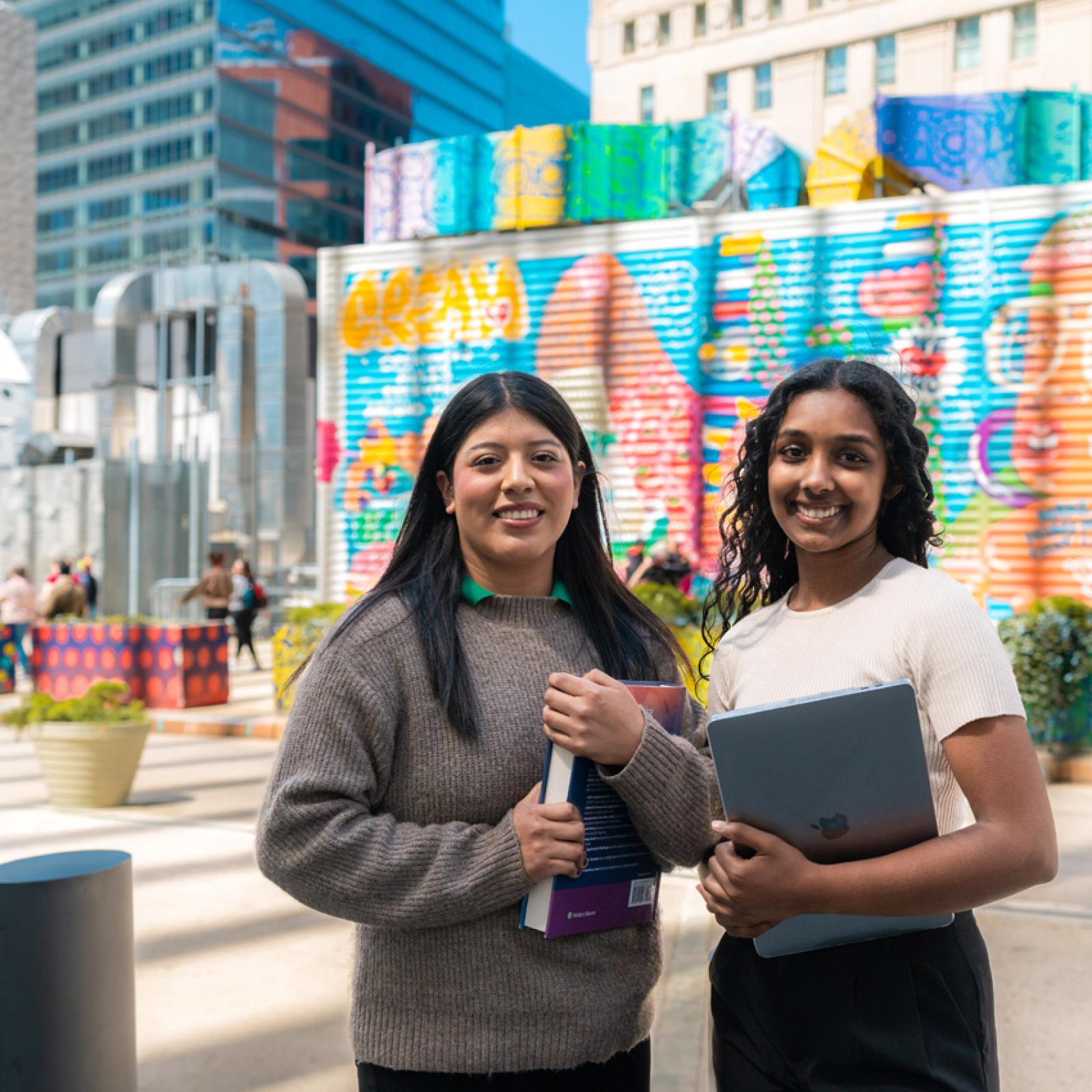 Two women standing in front of a famous graffiti mural. 