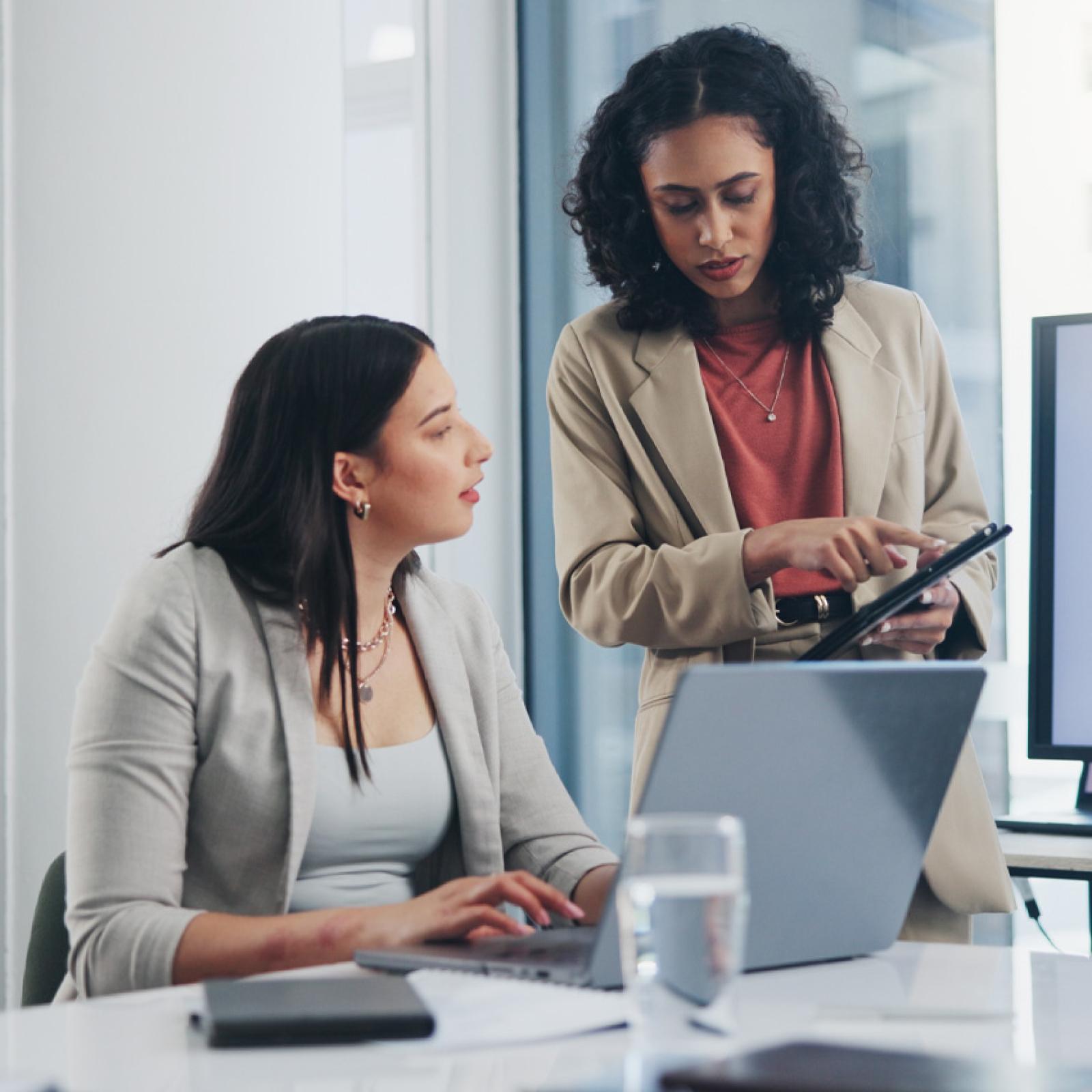 Two professional women speaking to each other in an office. 