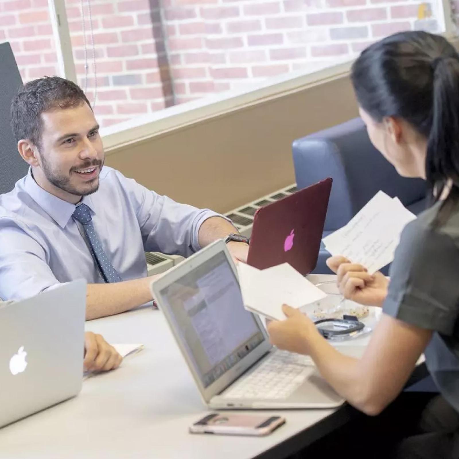 Pace University students working at a desk with laptops. 