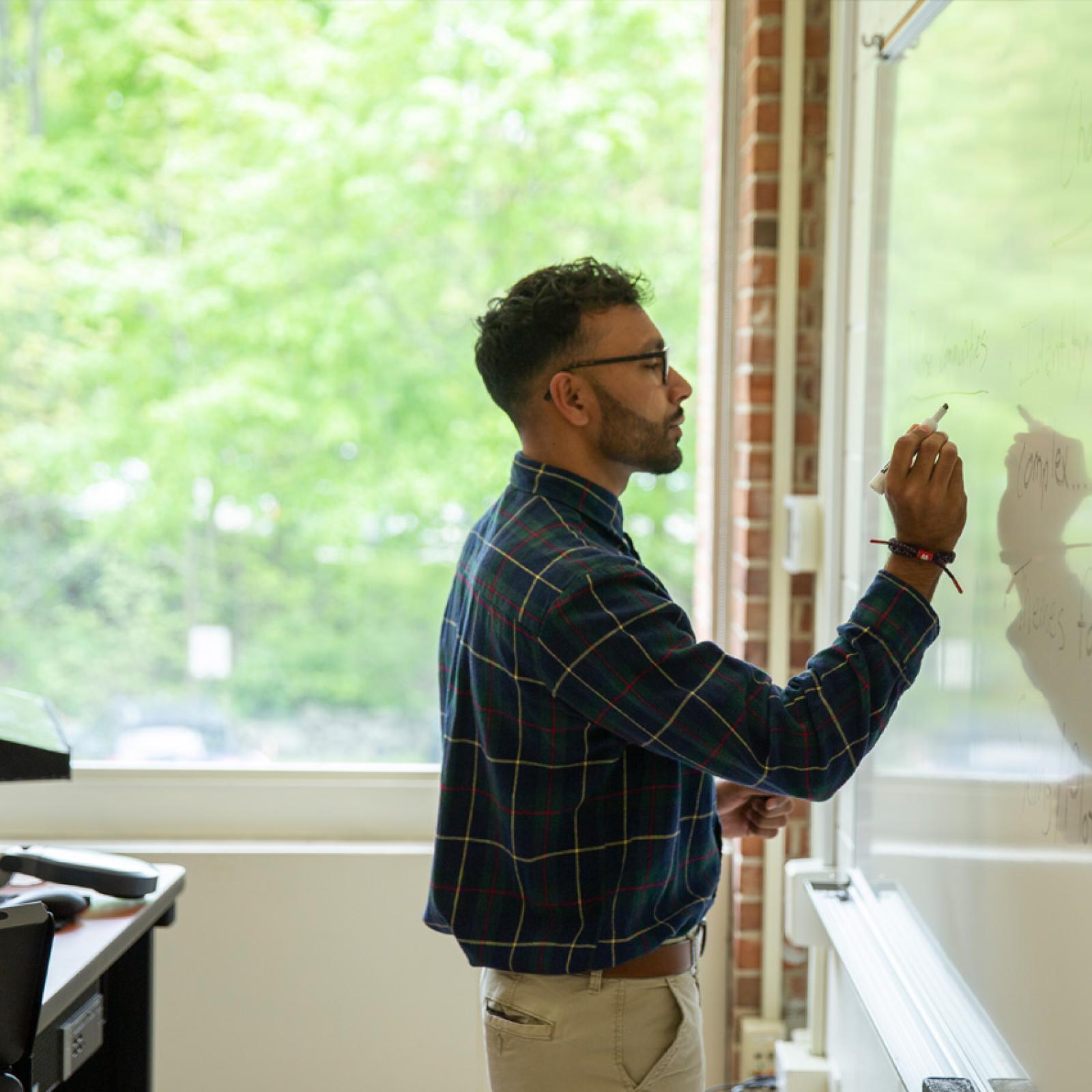 A teacher writing on a whiteboard in front of a window at Pace University.