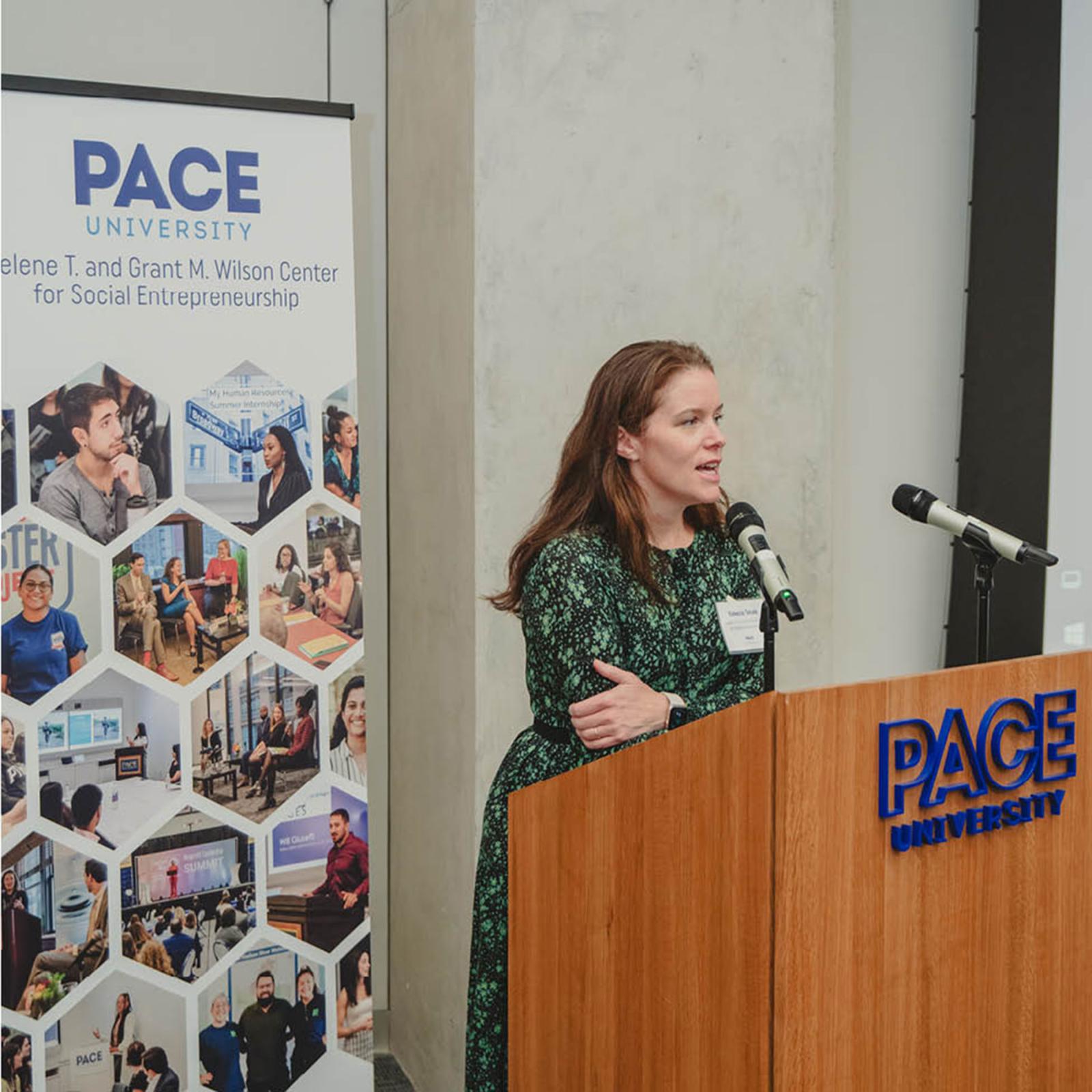 Pace University Public Administration professor Rebecca Tekula, PhD, standing behind a podium with a Wilson Center banner behind her