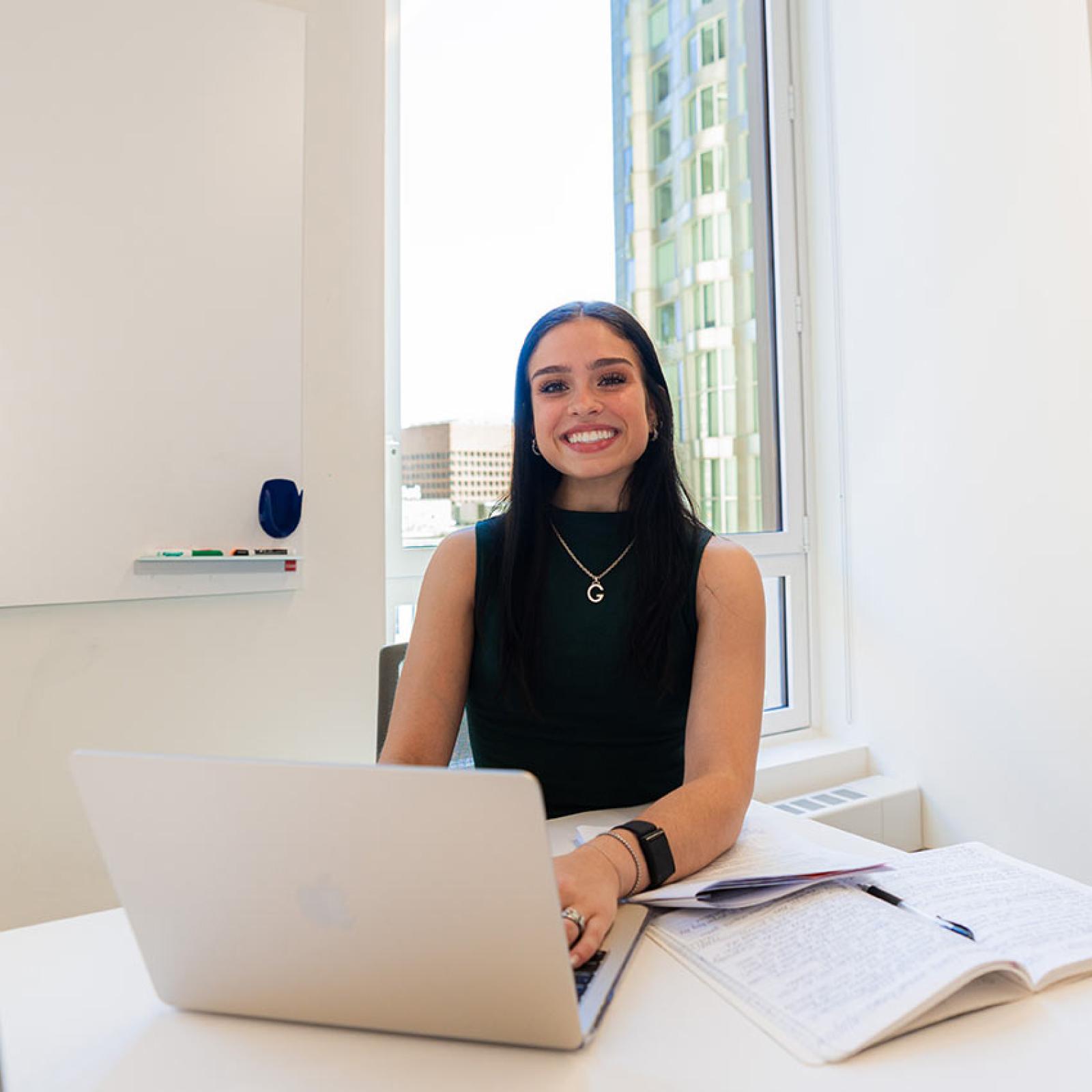 A Pace University student works on her laptop and smiles.