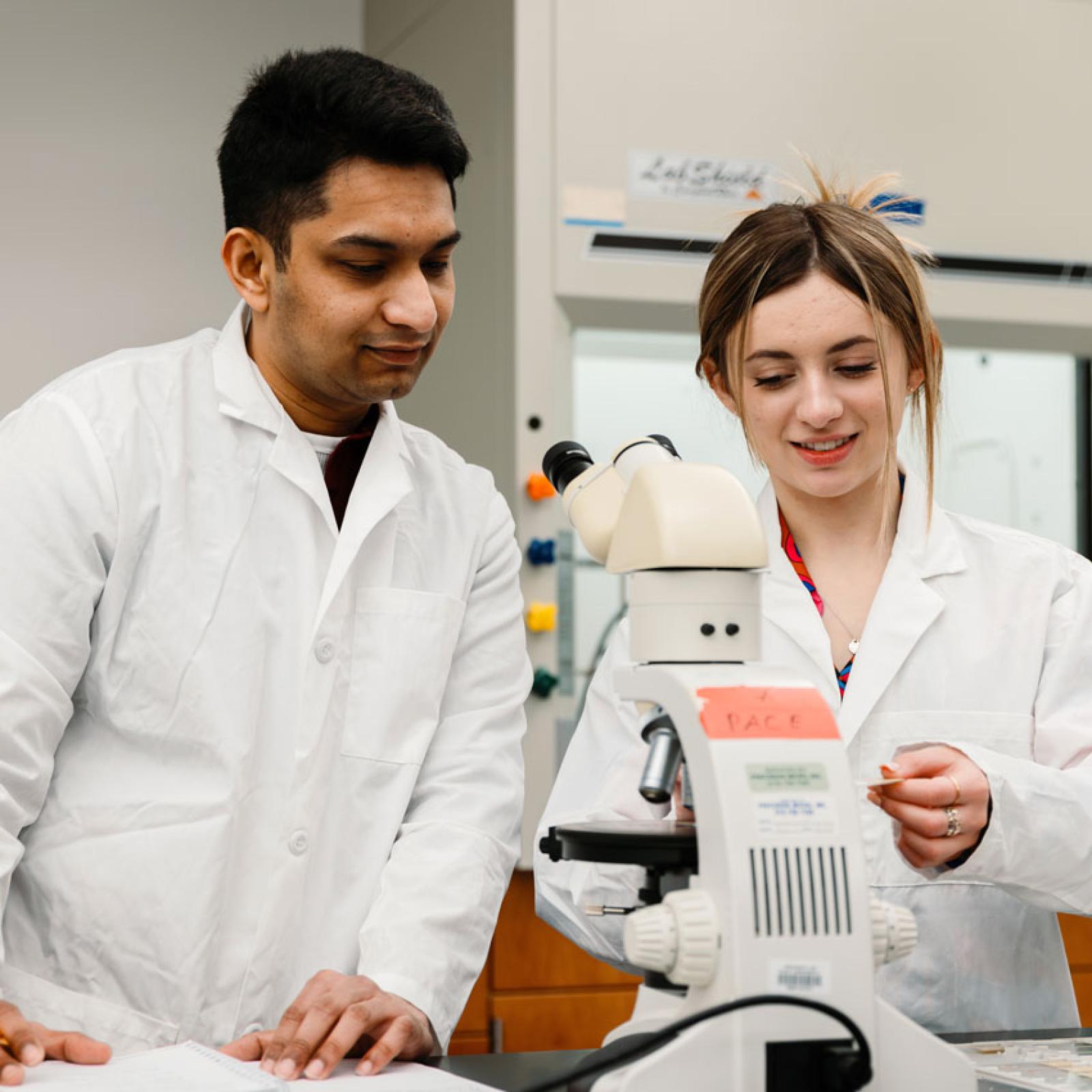 Pace University students in the lab looking at a microscope.