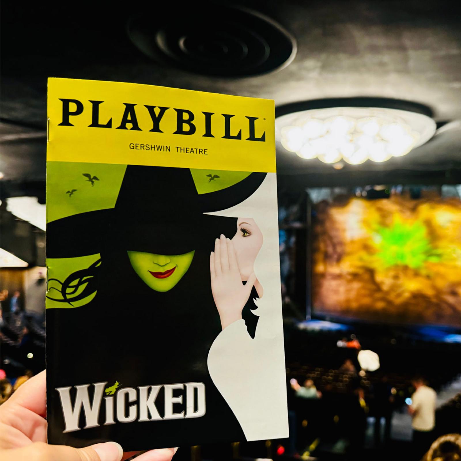 A hand holding a playbill for Wicked inside the theater. 